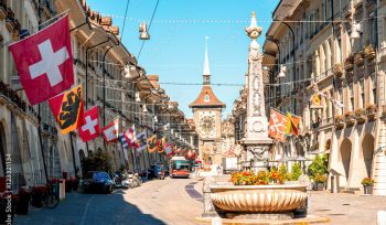 Street view on Kramgasse with fountain and clock tower in the old town of Bern city. It is a popular shopping street and medieval city centre of Bern, Switzerland